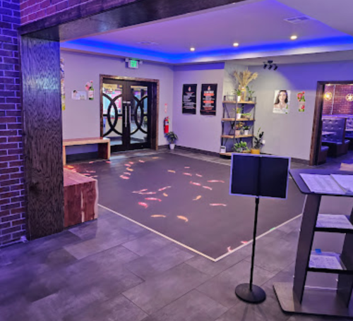 A modern entryway with a dark floor, colorful lights, seating, and decorative plants, featuring a welcoming atmosphere.