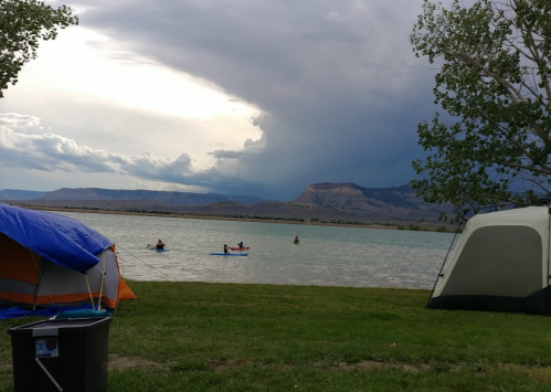 A campsite by a lake with tents, people kayaking, and dark clouds in the sky.
