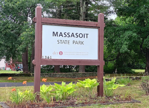 Sign for Massasoit State Park, featuring the park's name and logo, surrounded by greenery and flowers.