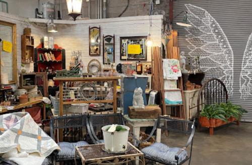 A cozy vintage shop filled with eclectic decor, furniture, and plants, featuring a whimsical wing mural on the wall.