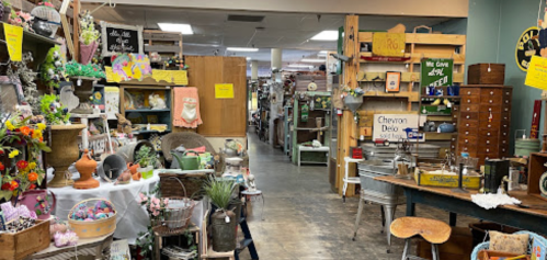 A vintage shop aisle filled with various antiques, decor items, and furniture, creating a cozy, eclectic atmosphere.