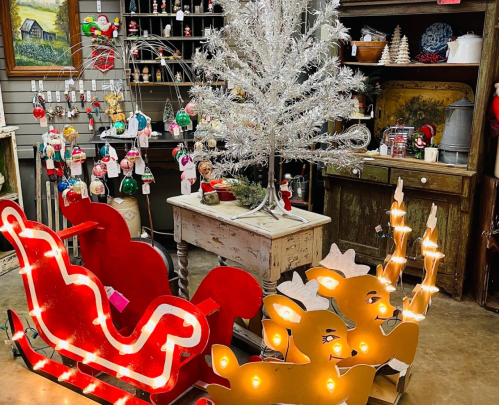 A festive display featuring a silver Christmas tree, a red sleigh, and illuminated reindeer decorations in a cozy shop.