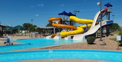 Colorful water slides at a pool area, with clear blue water and sunny skies in the background.