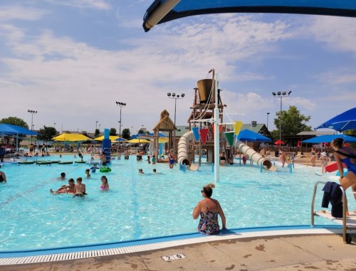 A busy water park with children swimming, water slides, and colorful umbrellas on a sunny day.