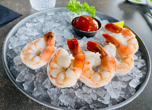 A platter of shrimp on ice, served with cocktail sauce and a lemon wedge, garnished with parsley.