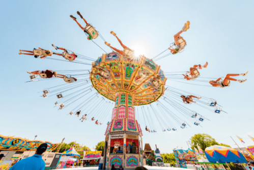 A colorful swing ride at a fair, with riders soaring through the air against a bright blue sky.