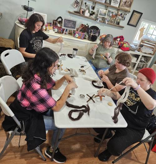 A group of five people sitting at a table, engaged in a crafting activity with various materials.