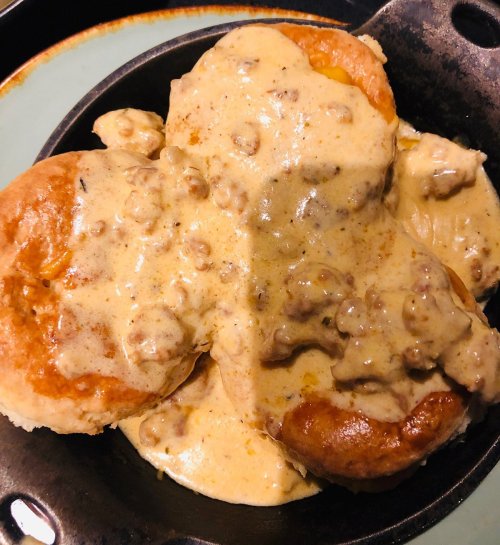 A close-up of biscuits topped with creamy sausage gravy in a cast iron skillet.