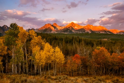 Golden sunlight illuminates rugged mountains, surrounded by vibrant autumn foliage in a serene landscape.