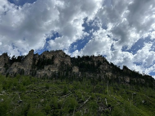 A rugged mountain landscape with towering cliffs, lush greenery, and a dramatic sky filled with clouds.