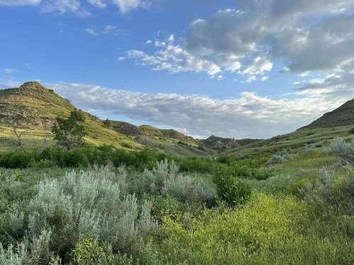 Lush green hills under a blue sky with scattered clouds, showcasing a serene natural landscape.