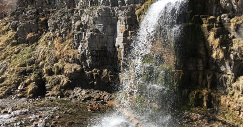 Water tumbles over a rocky ledge and into a shallow natural pool in a Utah canyon.