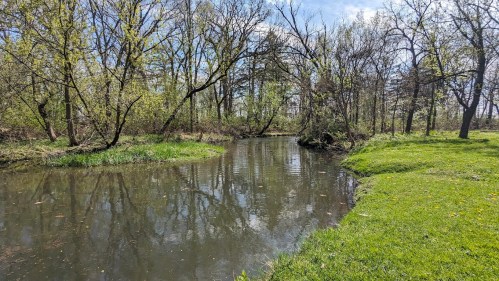 A serene river flows through a lush green landscape, surrounded by trees and reflecting the blue sky.