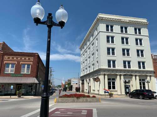 A street view featuring a vintage lamppost, a brick building, and a large white hotel under a clear blue sky.