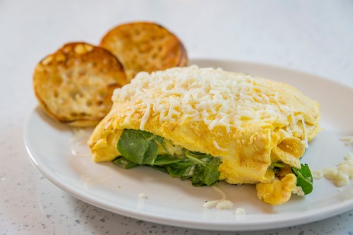 A fluffy omelette filled with spinach and topped with shredded cheese, served with toasted bread on the side.