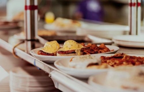 A close-up of a restaurant kitchen counter with plates of eggs Benedict and breakfast sides.