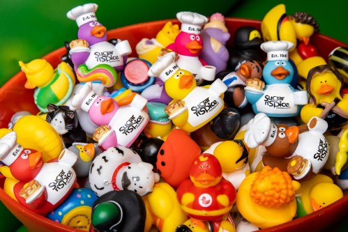 A colorful assortment of rubber ducks in chef hats, featuring various designs and themes, in a vibrant bowl.