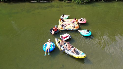 Aerial view of people relaxing on inflatable rafts and a kayak in a green river.