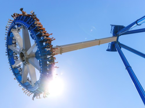A thrilling amusement park ride spins high against a clear blue sky, with excited riders hanging on.