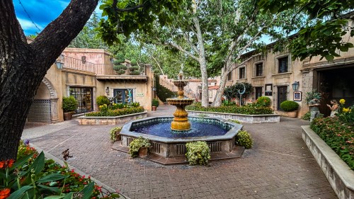 A charming courtyard with a central fountain, surrounded by lush greenery and quaint buildings.