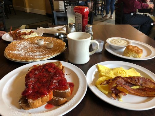 A table set with breakfast items: pancakes, bacon, French toast with strawberries, an omelet, and a biscuit with gravy.