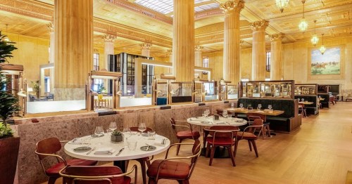 Elegant restaurant interior with tall columns, stylish seating, and well-set tables under a grand ceiling.