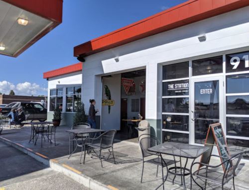 A modern café with outdoor seating, featuring large windows and a sign that reads "Polly" on a sunny day.