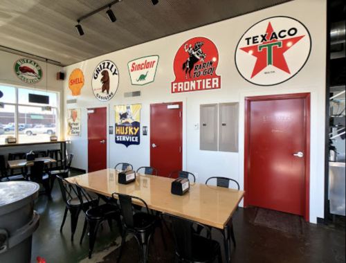 A dining area with a long wooden table and vintage gas station signs on the wall, featuring brands like Texaco and Sinclair.