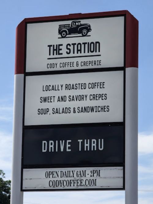 Sign for The Station featuring coffee, crepes, soup, salads, and sandwiches. Drive-thru available. Open daily 6 AM - 2 PM.