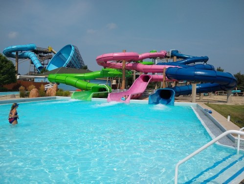 A water park featuring colorful slides and a clear blue pool, with a person swimming nearby.
