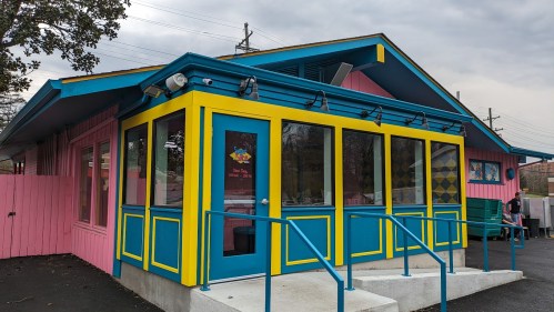 Colorful building with pink and blue exterior, large windows, and a welcoming entrance.