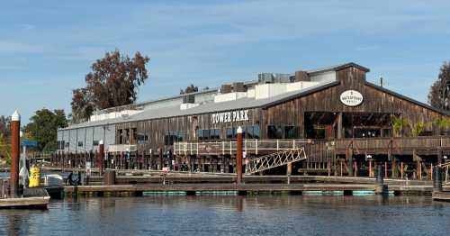 A wooden restaurant building by the water, featuring a deck and signage for "Tower Park." Clear blue sky above.