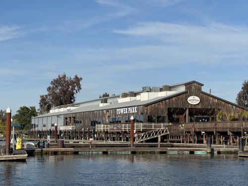 A wooden building labeled "Tower Park" by the water, with a clear blue sky and trees in the background.