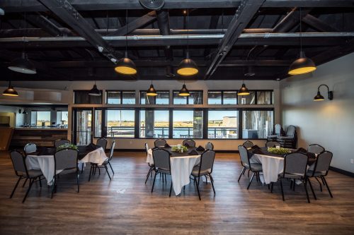 A spacious event room with round tables set for dining, large windows, and modern lighting fixtures.