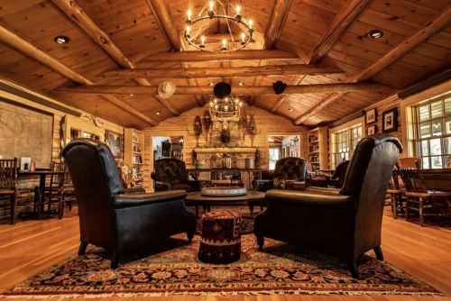 Cozy rustic living room with wooden beams, leather chairs, a stone fireplace, and decorative wall art.
