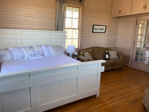 Cozy bedroom with a white bed, a brown couch, and large windows letting in natural light.