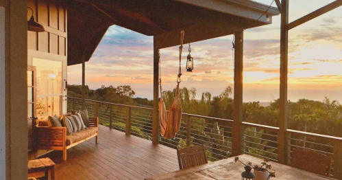 A cozy porch with a hammock, wooden furniture, and a stunning sunset view over lush greenery.