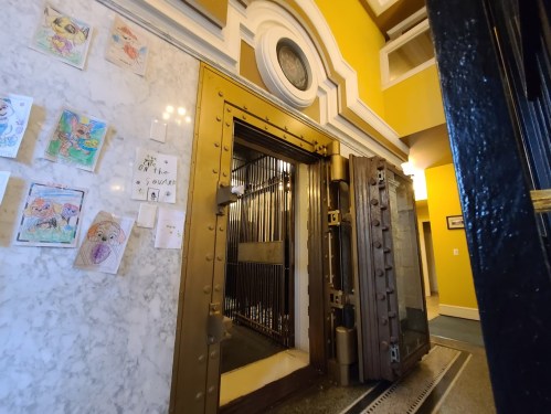 A large, open vault door in a brightly colored hallway, with children's drawings displayed on the wall nearby.