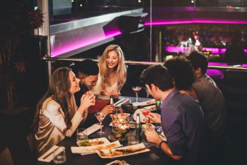 A group of friends enjoying dinner and drinks at a stylish restaurant, laughing and sharing a lively conversation.