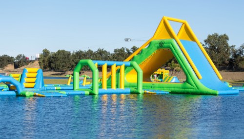 Colorful inflatable water park with slides and obstacles on a lake under a clear blue sky.