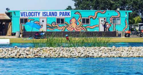 Colorful building with an octopus mural at Velocity Island Park, surrounded by water and greenery. People enjoying the area.