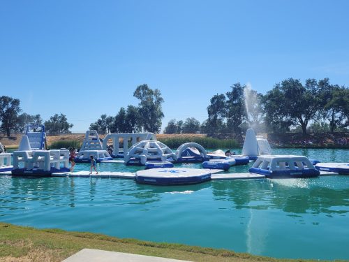 A water park with inflatable structures on a lake, featuring people playing and enjoying the sunny day.