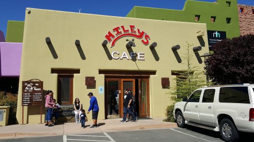 Exterior of Miley's Cafe with people outside, colorful buildings in the background, and a white SUV parked nearby.
