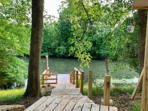 A wooden dock leads to a serene, green lake surrounded by lush trees.