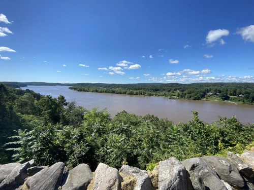 A scenic view of a river surrounded by lush greenery and blue skies with scattered clouds.