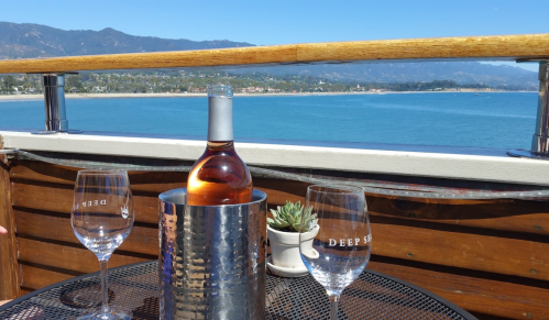 A bottle of rosé in an ice bucket with two glasses, overlooking a scenic coastal view.