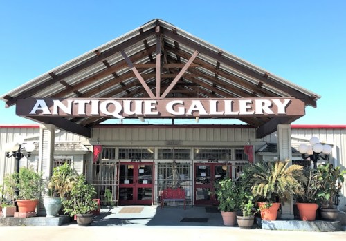 Exterior of an antique gallery with a wooden sign, large entrance, and potted plants under a clear blue sky.