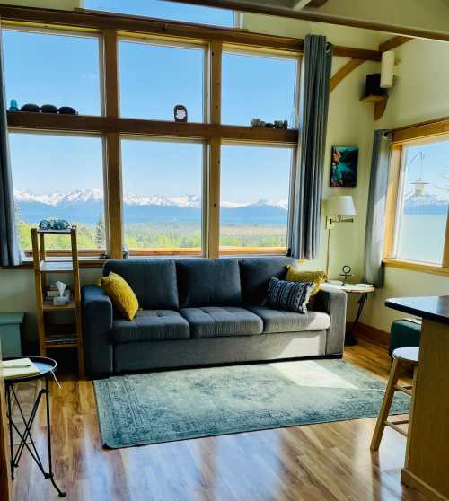 Cozy living room with a gray sofa, large windows showcasing a mountain view, and warm wooden accents.