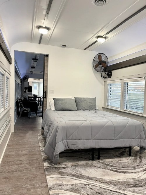 Cozy interior of a modern space with a bed, rug, and dining area, featuring large windows and stylish decor.