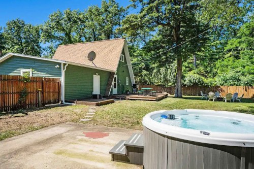 A backyard with a hot tub, green house, and wooden deck surrounded by trees and a wooden fence.